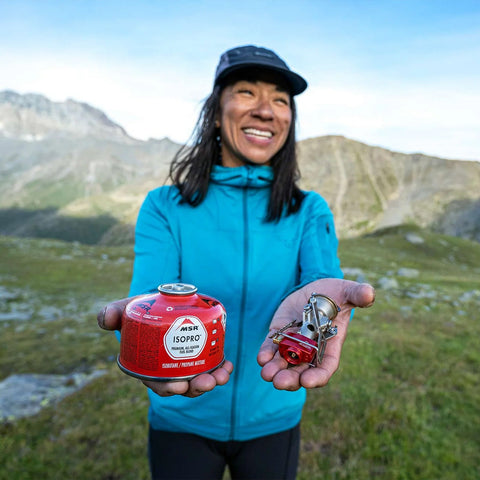 Bergsteigerin präsentiert MSR Isopro Brennstoffkanister und Campingkocher, ideal für Outdoor-Abenteuer und Trekking in den Bergen.