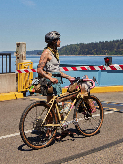 Alt-Text (Deutsch):
Abenteurerin mit Swift Industries Bikepacking-Ausrüstung am Wasser.
