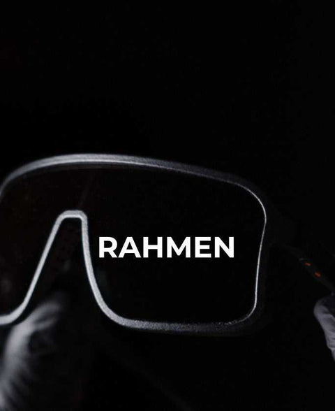 Nahaufnahme einer Sportbrille mit schwarzem Rahmen vor dunklem Hintergrund, mittig mit dem weißen Schriftzug „RAHMEN“ über dem Glas.