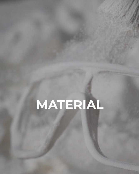 Schutzbrille mit weißem Pulver bedeckt, im Hintergrund unscharfes Material und Pinsel – Fokus auf das Thema Materialbearbeitung oder Sicherheitsausrüstung.