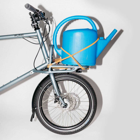 Compact Cargobike Flinc mit blauer Gießkanne auf Frontträger. Praktisch für Gartenfreunde und urbane Lieferdienste.