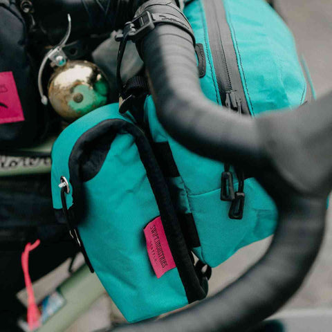 Türkise Swift Industries Kestrel Handlebar Bag 2L am Fahrradlenker montiert. Praktisches Zubehör für Bikepacking-Abenteuer.