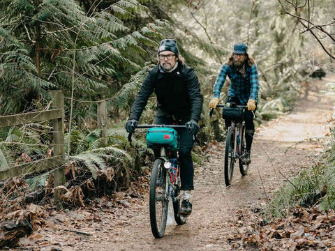 Zwei Radfahrer mit Swift Industries Kestrel Handlebar Bag 2L auf Waldweg. Ideale Lenkertasche für Abenteuer und Naturfahrten.