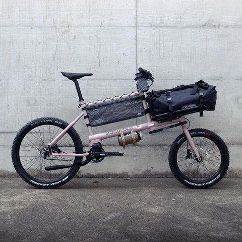 Rosa Monopole E-Bike mit robustem Rahmen, 29-Zoll Reifen, Gepäckträger, in Innenraum auf weißer Wand mit Betonboden präsentiert
