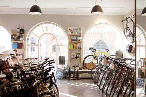 Heller Fahrradladen mit modernen Rennrädern, Citybikes und Zubehör, großen Rundbogenfenstern und stilvoller Einrichtung im urbanen Stil.