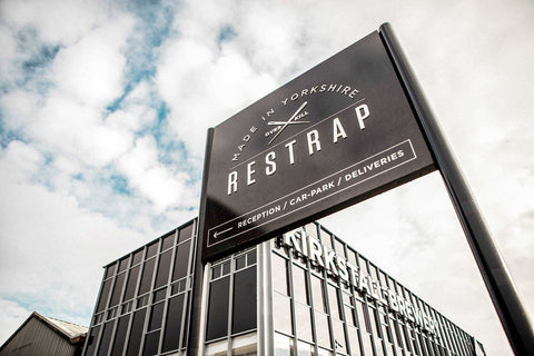 Firmenschild von Restrap mit der Aufschrift „Made in Yorkshire – Restrap – Original Kit“ vor einem modernen Industriegebäude mit Glasfassade und dem Schriftzug „WORKSPACE“.