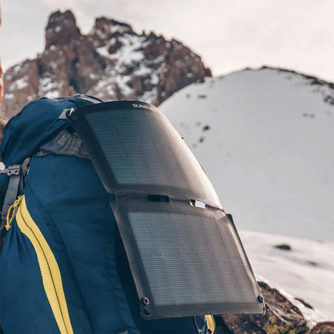 Tragbares, dunkles Solarpanel auf einem Rucksack in verschneiter Berglandschaft, ideal für unterwegs, langlebig und effizient