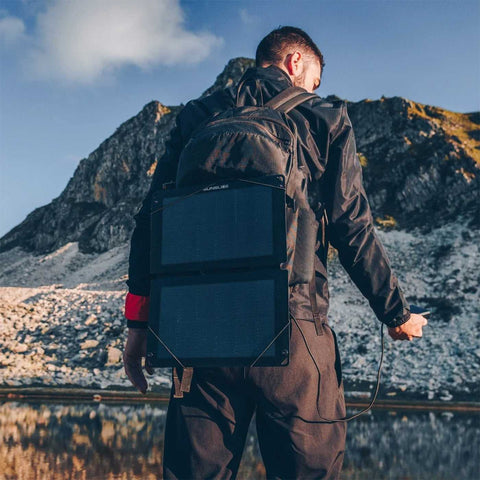 Mann mit Rucksack und Solar-Panel auf einem Bergpfad, lädt sein Smartphone, umweltfreundliche Energiequelle, leichte Tragbarkeit