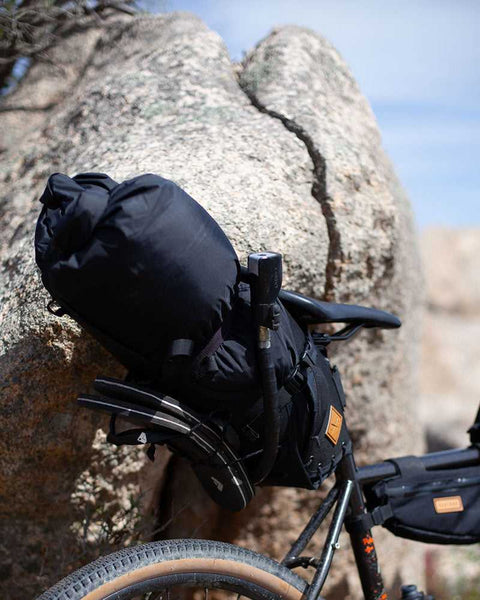 Fahrrad mit umfangreicher Bikepacking-Ausrüstung, darunter große schwarze Gepäcktaschen am Lenker und Rahmen, vor einem Felsen in einer trockenen, felsigen Landschaft.