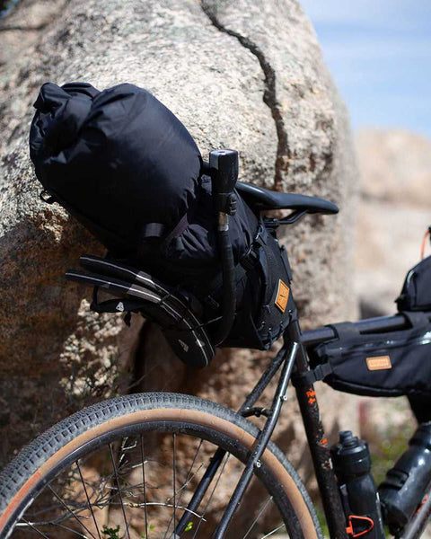 Fahrrad mit Bikepacking-Ausrüstung, darunter eine große schwarze Satteltasche, befestigt am Sattel und Sattelstütze, vor einem Felsen in natürlicher Umgebung.