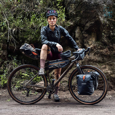 Bikepacking-Abenteurerin mit Ortlieb Seat-Pack Saddle Bag und weiteren Taschen auf einem Gravelbike, bereit für Offroad-Touren.