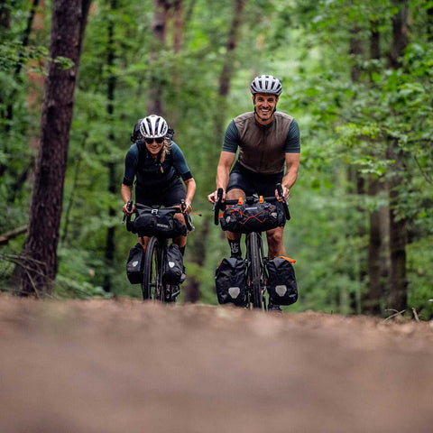Zwei Radfahrer mit Ortlieb Handlebar-Pack Taschen auf Waldweg, ideal für Bikepacking und Outdoor-Abenteuer.