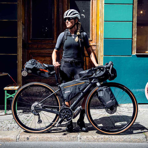 Fahrradfahrerin mit kompletter Ortlieb Bikepacking-Ausrüstung inklusive Frame-Pack 6L, bereit für Abenteuer in der Stadt oder Natur.