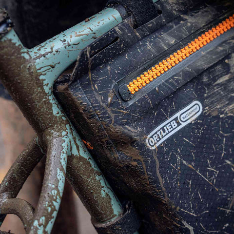 Ortlieb Frame-Pack 6L in schwarz matt mit Schlammspritzern, zeigt strapazierfähiges, wasserdichtes Material für extreme Outdoor-Bedingungen.